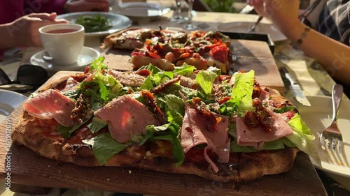 Gourmet pizza with mortadella, fresh greens and sun dried tomatoes on a wooden board in warm sunlight