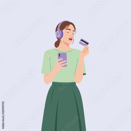 Young woman with working headphones holds credit card and mobile phone, enjoying music. Working headphones lets girl to buy online, shop, booking app, and making payments.