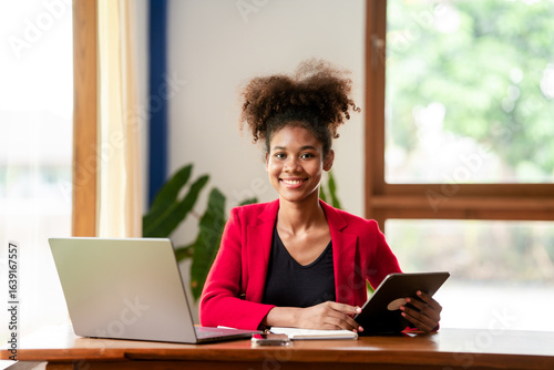 Young African American Woman Working Online with Laptop and Tablet at Home Office Smiling in Red Suit for Business and Technology