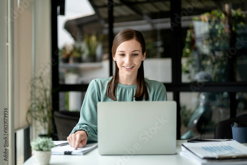 Free Download Young Businesswoman Working on Laptop Computer in Modern Office Caucasian Female Professional Smiling at Desk Doing Research Online Analyzing Data for Project Success - GFXLoad