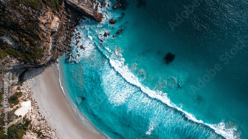 A stunning top-down drone shot captures the raw power of ocean waves against a scenic and rocky shore.