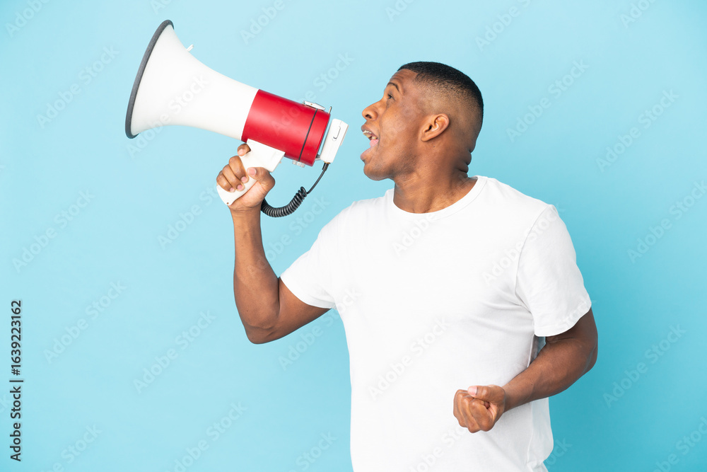 Young latin man isolated on blue background shouting through a megaphone to announce something in lateral position Young latin man isolated on blue background shouting through a megaphone to announce something in lateral position