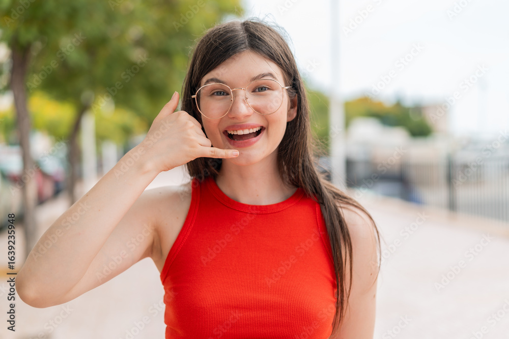 Young woman with glasses at outdoors making phone gesture. Call me back sign Young woman with glasses at outdoors making phone gesture. Call me back sign
