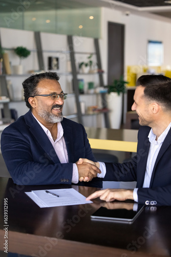 Billede på lærred Happy business project buyer and seller men shaking hands, sitting at work table with documents, meeting for cooperation, partnership, getting agreement about investment