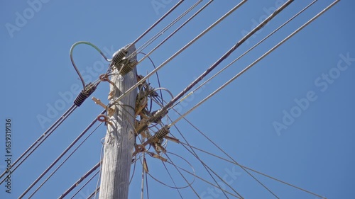 Wooden pole wired with electricity cables under a clear blue sky in a sunny outdoor setting, showcasing an essential infrastructure element in a rural environment.