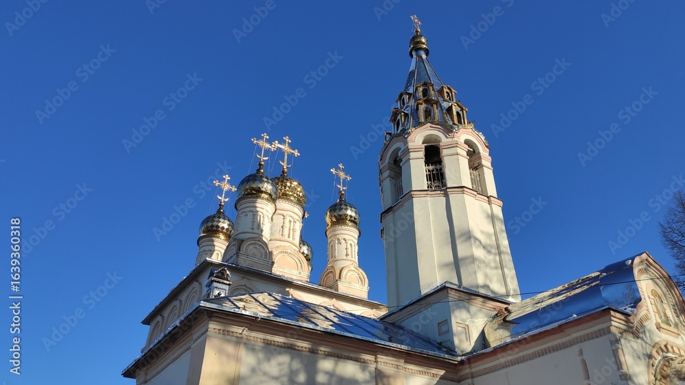 Fototapeta premium A breathtaking low-angle view of the golden domes and bell tower of an Orthodox church against a clear blue sky, capturing the purity of divine light and unwavering faith.