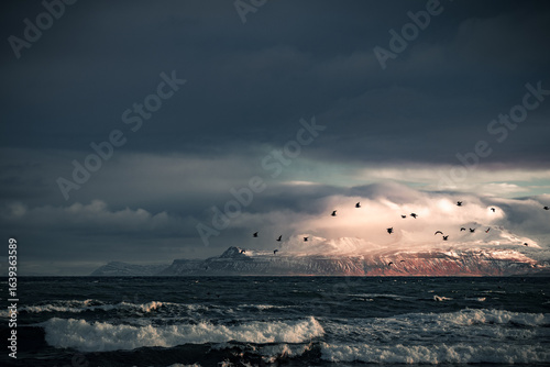 Dramatic view of the stormy sea along the Snæfellsnes Peninsula in Iceland, captured at sunset. Powerful waves crash against the rugged coastline under golden light, creating a striking contrast betwe