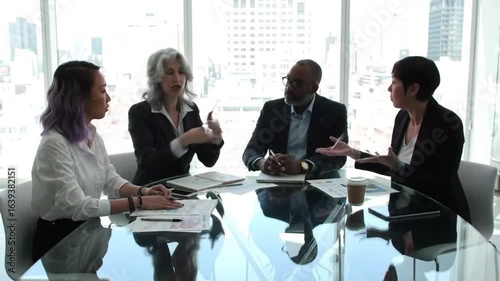 A diverse group of professionals collaborates around a reflective glass table during a business meeting, discussing ideas and strategies.