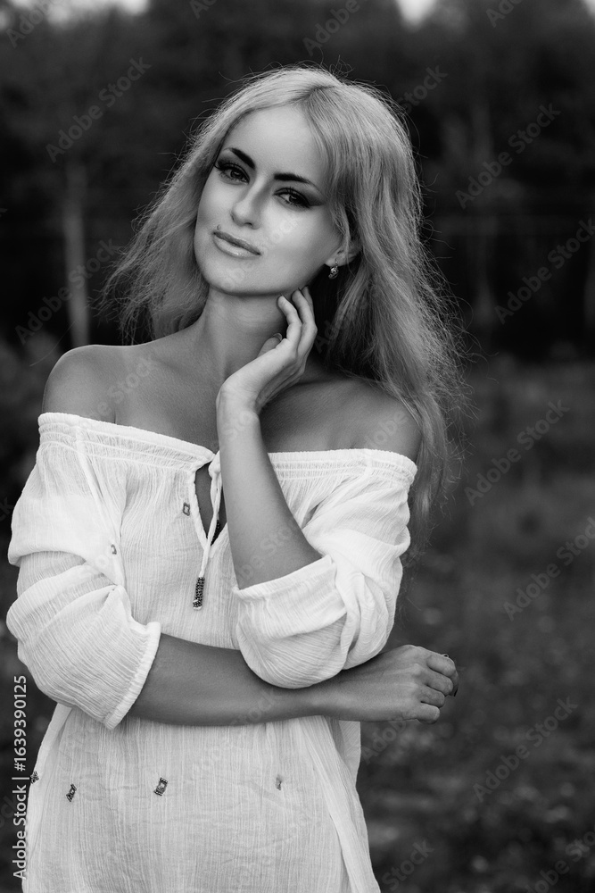 Obraz premium Portrait of a young beautiful blonde girl in light clothes outdoors in summer. Black and white photo.
