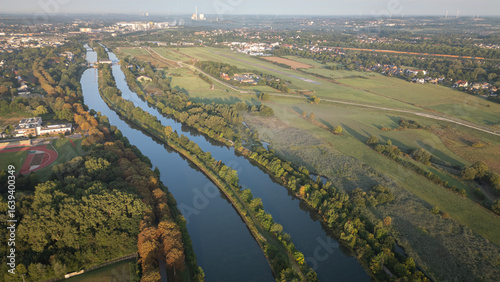 Aerial panoramic view of a river meandering through green fields and rural landscapes in Germany during sunrise, captured by drone.