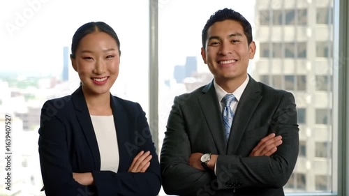 Two smiling professionals stand side by side, radiating confidence and success, in front of a bright window with a city view.