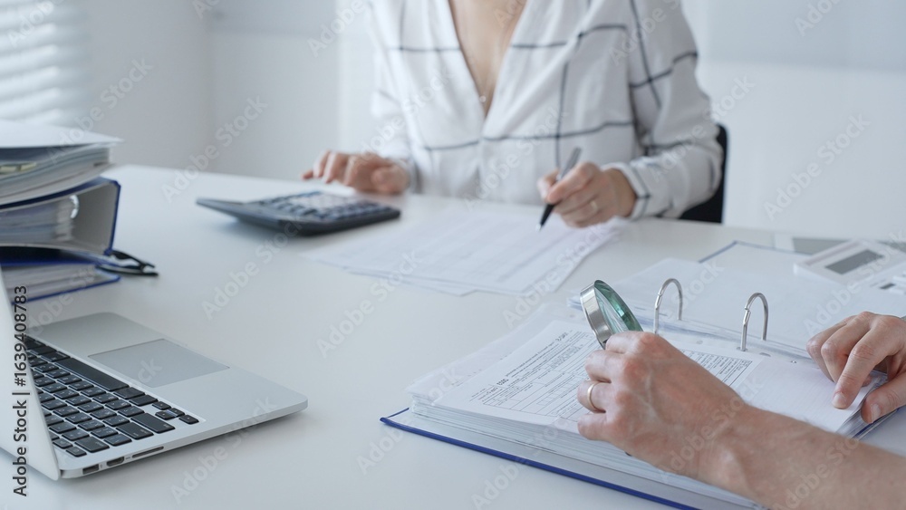 Fototapeta premium Team of professional accountants working together, using a magnifying glass and a calculators, to audit financial reports in their brightly lit office. Audit and taxes in business