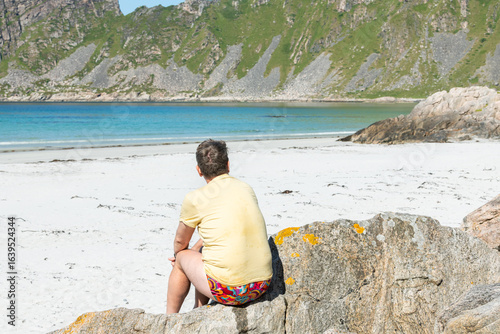 Papier peint Backview of a caucasian tourist sitting on a rock an looking at Høyvika Beach, a beautiful sandbeach in Vesteralen, Vesterålen islands in arctic Norway