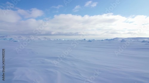 Wallpaper Mural Gliding over a vast, wind-swept Antarctic ice field with distant mountains under a blue sky. Torontodigital.ca