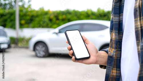 Man holds smartphone with white screen near luxury car, perfect for mobile app promotions and tech-savvy drivers