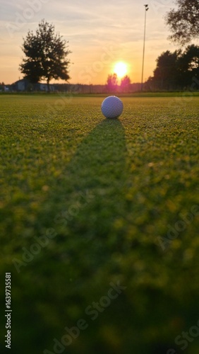 golf ball on tee. Golf ball positioned on the green in the warm glow of a sunset, with a long shadow stretching toward the camera.