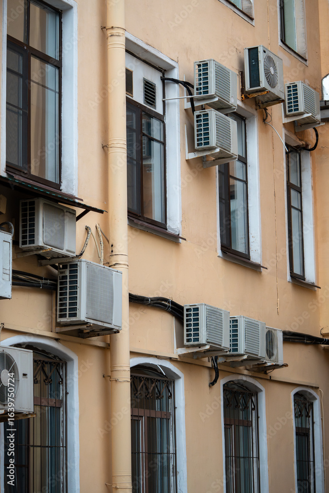 Facade of building with many air conditioners on windows in southern hot country. Yellow house exterior on city street. Escape from heat, creating favorable microclimate in urban apartments concept. Facade of building with many air conditioners on windows in southern hot country. Yellow house exterior on city street. Escape from heat, creating favorable microclimate in urban apartments concept.