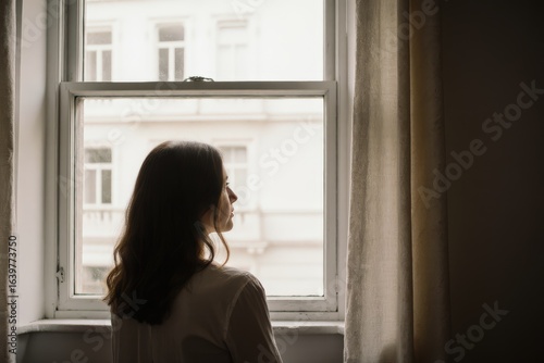 Woman at home, looking out of window, rear view