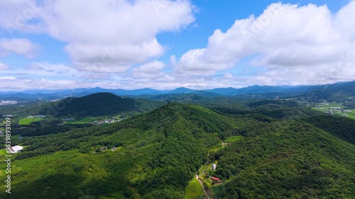 Aerial Drone View of Highway and Cars Driving Through Green Fields and Forest, with Vast Summer Landscape, Blue Sky, and Clouds for a Healing Scenery