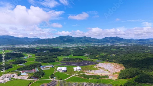 Aerial Drone View of Highway and Cars Driving Through Green Fields and Forest, with Vast Summer Landscape, Blue Sky, and Clouds for a Healing Scenery