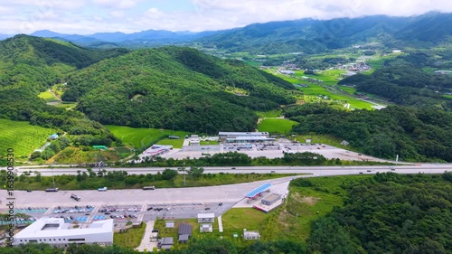 Aerial Drone View of Highway and Cars Driving Through Green Fields and Forest, with Vast Summer Landscape, Blue Sky, and Clouds for a Healing Scenery