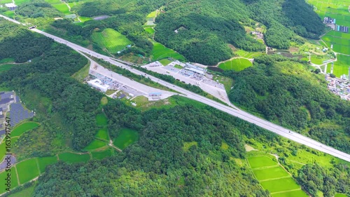 Aerial Drone View of Highway and Cars Driving Through Green Fields and Forest, with Vast Summer Landscape, Blue Sky, and Clouds for a Healing Scenery