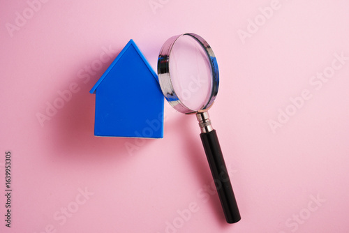 Magnifying glass with blue toy house on pink background