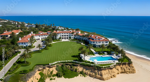 Aerial view of a large white mansion with a red tile roof overlooking the ocean and a swimming pool