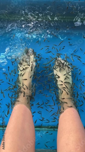 Top-down close-up of feet in fish spa aquarium with fish doing peeling treatment