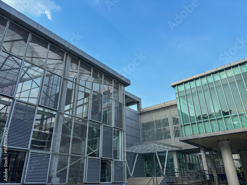 modern architectural shot of a contemporary building with large glass windows and metal louvers against a blue sky, showcasing a clean, institutional design.