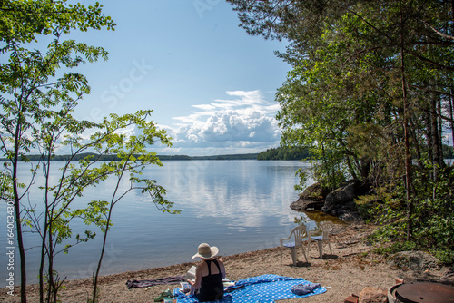 Canvastavla Woman sitting on the beach at lake Saimaa in Finland