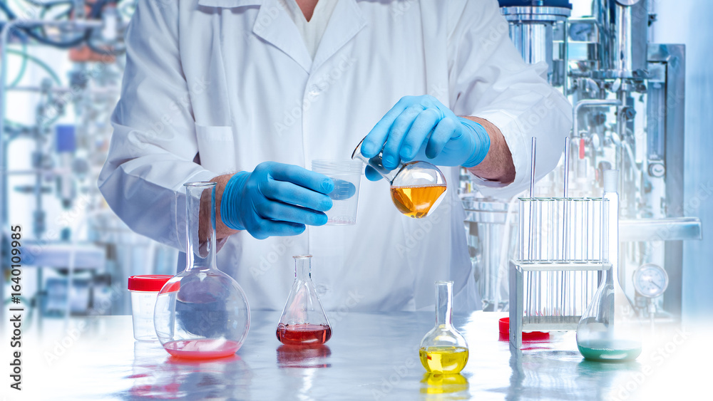 Fototapeta premium Scientist in lab coat and gloves pours liquid from flask during chemical experiment. Laboratory research, chemistry, biotechnology, innovation, science, and pharmaceutical work.