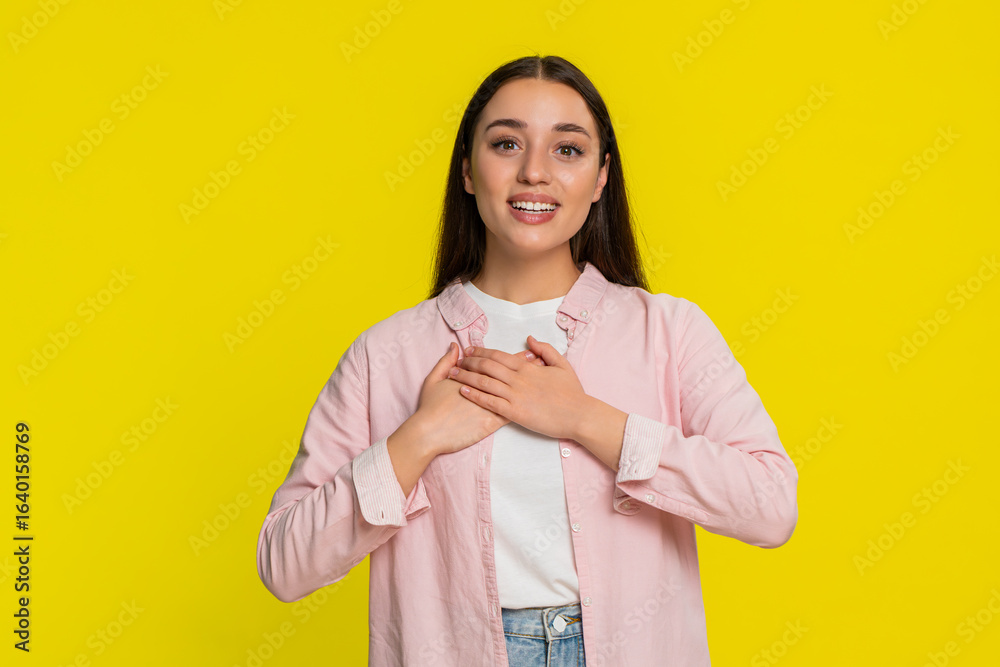 Young woman holding both hands on chest with raised eyebrows clearly expressing deep gratitude appreciation. Girl on yellow background shows heartfelt emotion and sincere thankful reaction with warmth Young woman holding both hands on chest with raised eyebrows clearly expressing deep gratitude appreciation. Girl on yellow background shows heartfelt emotion and sincere thankful reaction with warmth