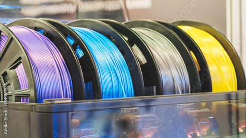 A row of multi-colored plastic tubes with blue, purple, yellow and green stripes for 3D printing. The tubes are arranged in a row and are located in a container.