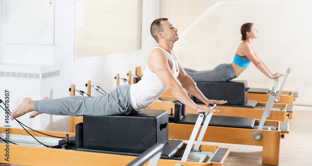 Obraz premium Sporty man in sports wear engages in Pilates on the reformer machine