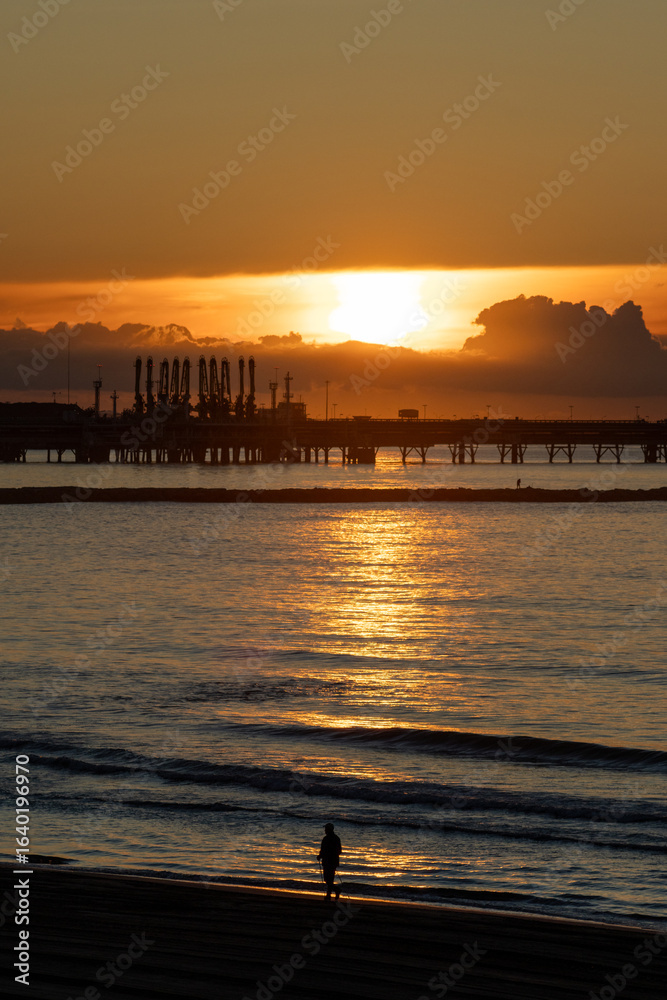 Naklejka premium Sunrise at Platja de la Pineda, Vila-seca, Tarragona, Catalonia, Spain, with views of the port and Tarragona’s cargo cranes over the Mediterranean Sea.