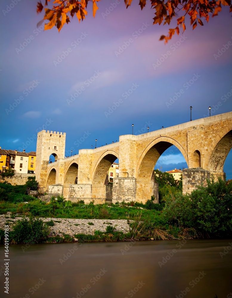 Fototapeta premium Ancient stone bridge over a river at sunset