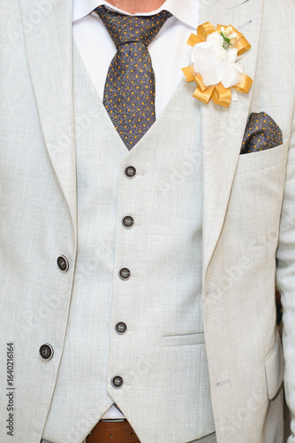 Faceless closeup of a groom with a decorative flower on his jacket lapel. A handkerchief in a jacket pocket. Shirt, tie, waistcoat and jacket.
