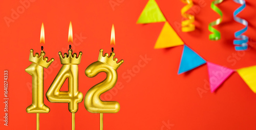 Number 142 birthday candle on an orange background with pennants