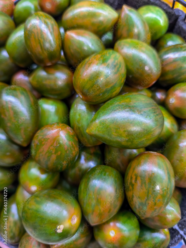 A bunch of green tomatoes are piled up in a basket. The tomatoes are of different sizes and are arranged in a way that they are not touching each other. The basket is placed on a table A bunch of green tomatoes are piled up in a basket. The tomatoes are of different sizes and are arranged in a way that they are not touching each other. The basket is placed on a table