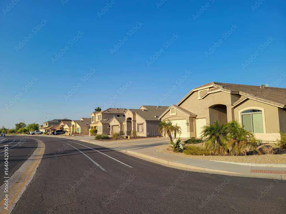 Obraz premium Arizona residential neighborhood with typical single family houses along curving street with xeriscaped roadside under clear blue sky in summer