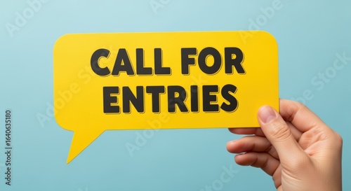 Hand Holding Yellow Speech Bubble with Call for Entries Message on Blue Background