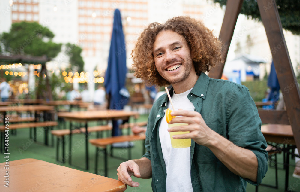 Fototapeta premium Happy latin man enjoying a refreshing cocktail in a lively beer garden setting