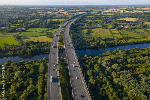 Aerial view of the M6 motorway on Thelwall Viaduct crossing the River Mersey near Warrington, surrounded by green fields, farmlands, and dense woodland