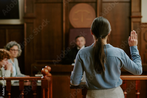 Schilderij op canvas Caucasian young adult woman standing in courtroom raising right hand while swear