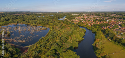 Aerial panoramic view of Woolston, near Warrington, with the River Mersey winding past residential areas, dense woodlands, and a wetlands