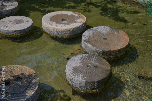 Ancient Stone Grinding Wheels Submerged in Shallow Water Creating a Natural Decorative Feature