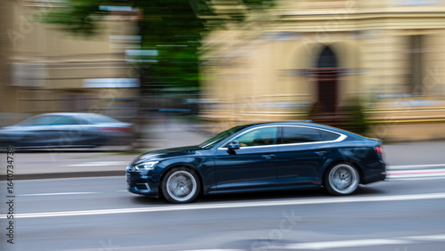 Bilde på lerret A black sedan is in motion, captured on a city street, creating a blurred background effect indicating speed