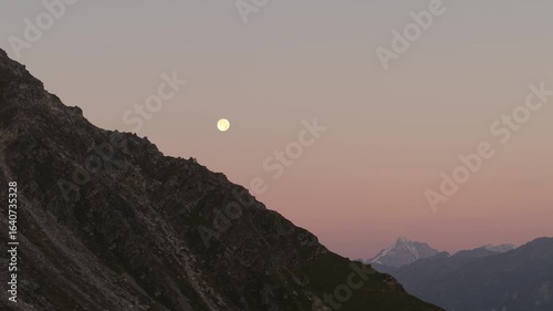 Close-up drone video of the Italian Alps in the morning, showing the moon in the sky and the Italian Dolomites in the distance.