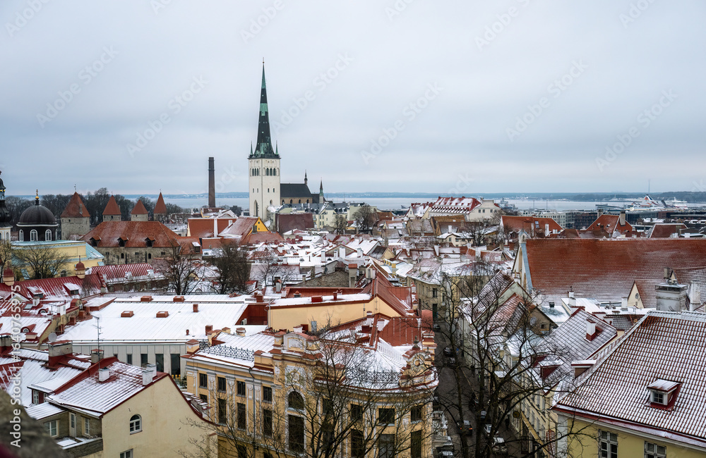 Naklejka premium Winter panoramic view of snowy rooftops and St Olaf church in Tallinn old town